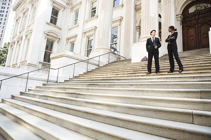 A well dressed man and woman converse on the steps of a legal or municipal building. Could be business or legal professionals or lawyer and client
